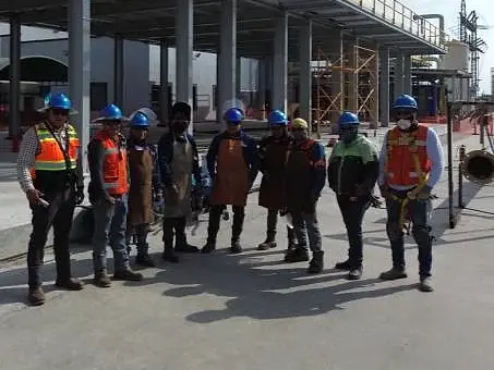 Cuadrilla de ingeniería con casco, chaleco y arnés frente a un rack de tubería